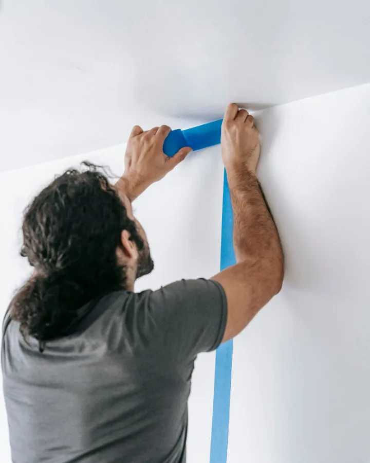 Schilder plakt met blauwe tape een strakke lijn af tussen wand en plafond