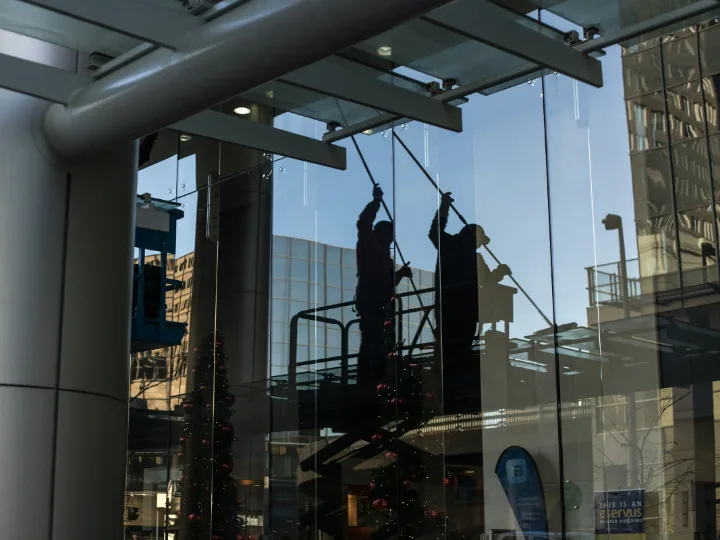 Glazenwassers op een hoogwerker achter een grote glazen pui
