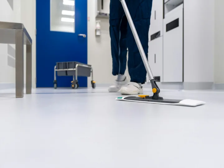 Iemand in blauwe kleding dweilt de witte vloer van een praktijkgang