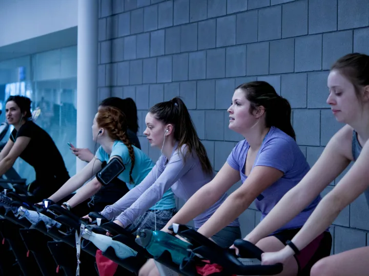 Een rij vrouwen fietst op spinningfietsen tegen een grijze muur
