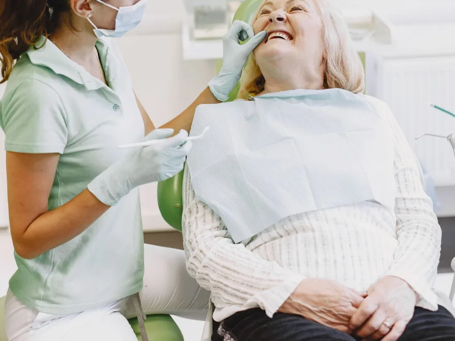 Een mondhygiënist behandelt een lachende oudere vrouw in de stoel