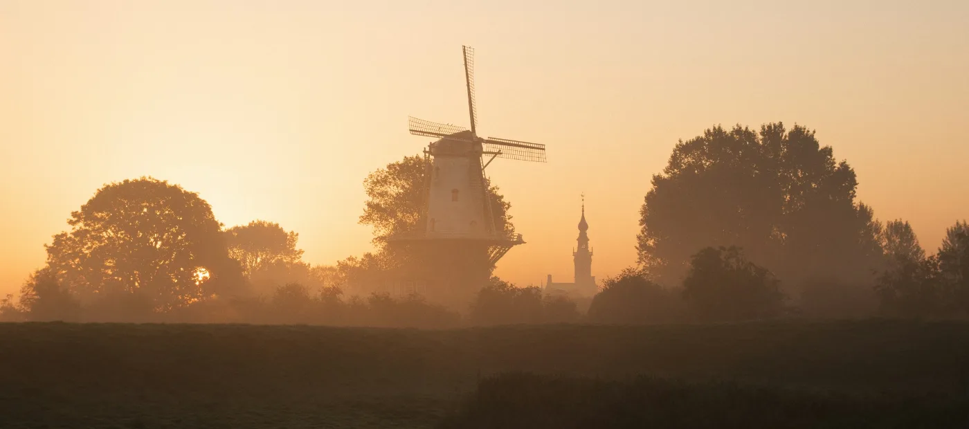 Een molen en een kerktoren in de ochtendmist boven het Friese land